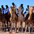 Colorfully attired riders on camels crossing sandy desert under clear skies