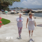 Two women in vintage dresses and hats strolling on a sunny beach