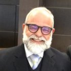 Elderly man with white mustache and glasses in black suit smiling on rocky backdrop