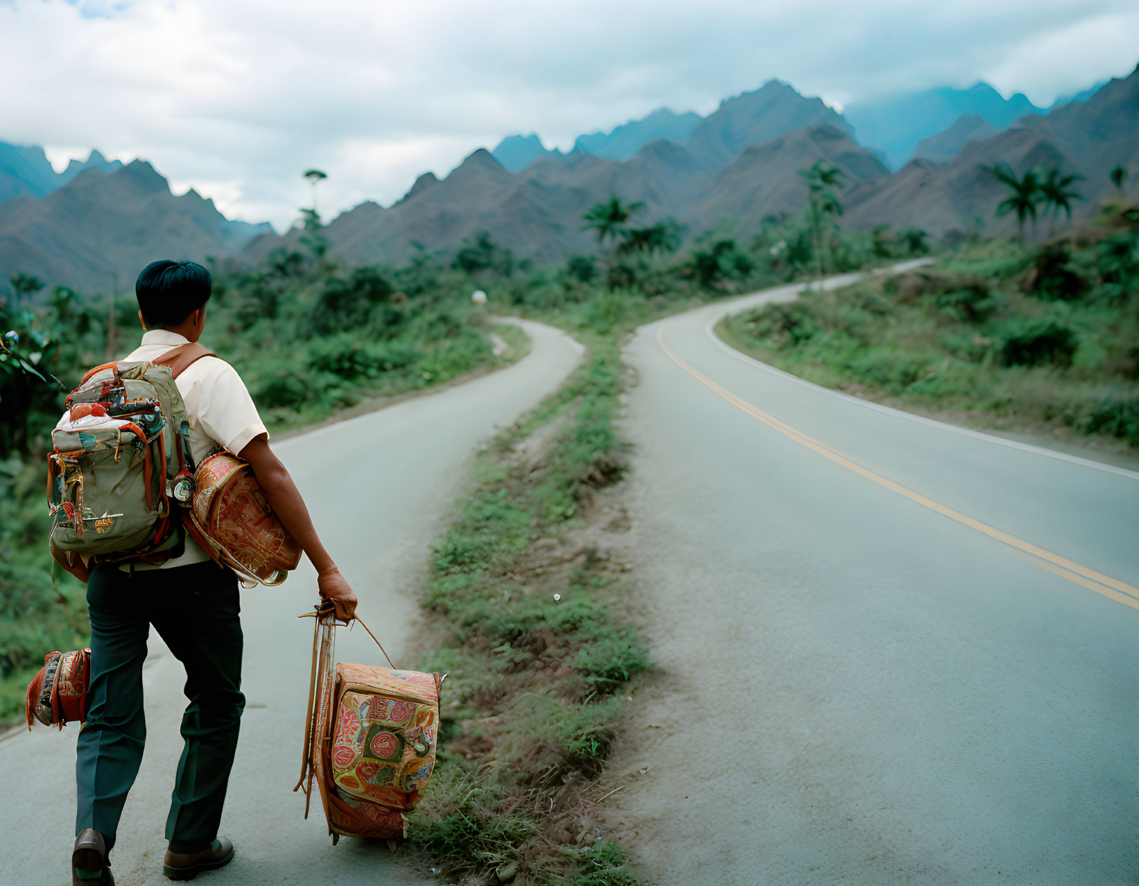 Hiker with backpack and patterned bag on mountain road