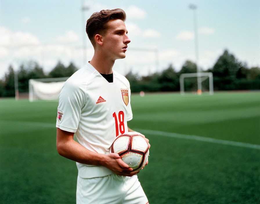 Young soccer player in white jersey with number 18 holding football on field