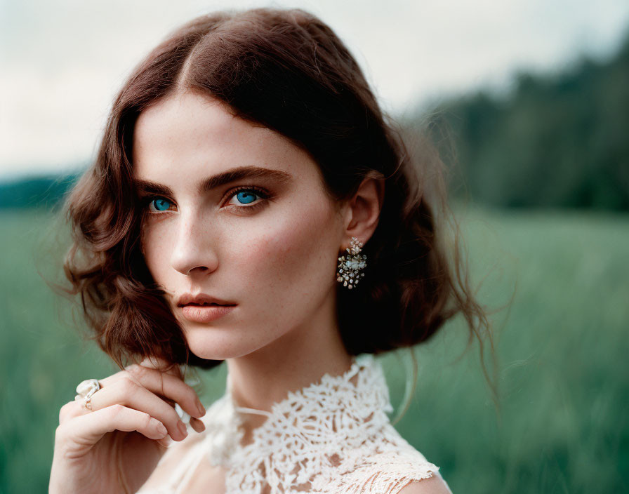 Brunette woman with blue eyes in white lace dress in green field