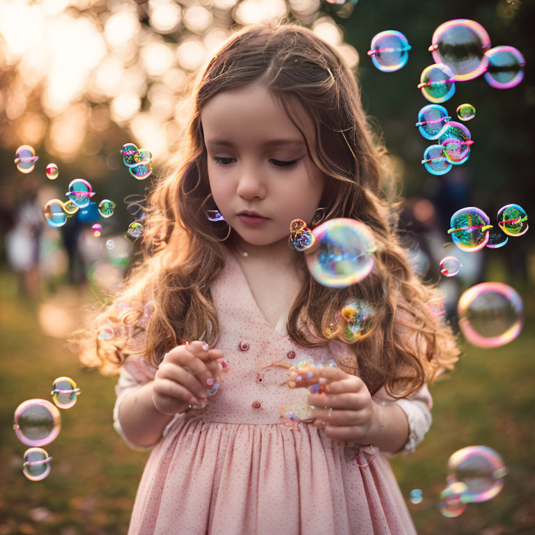 Young girl in pink dress captivated by floating soap bubbles in sunlit park