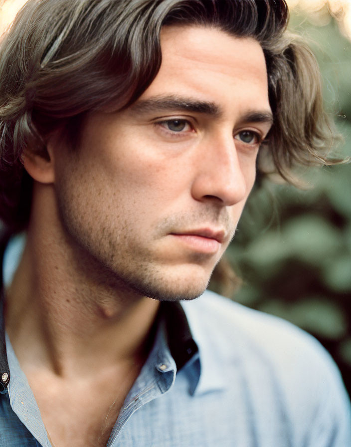 Young man with tousled hair and slight beard in contemplation against blurred natural backdrop