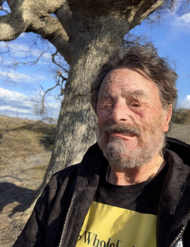 Elderly man with beard and smile under tree and blue sky