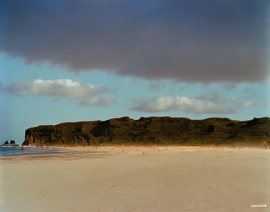 Tranquil beach scene with sandy shore, rock formations, and cloudy sky