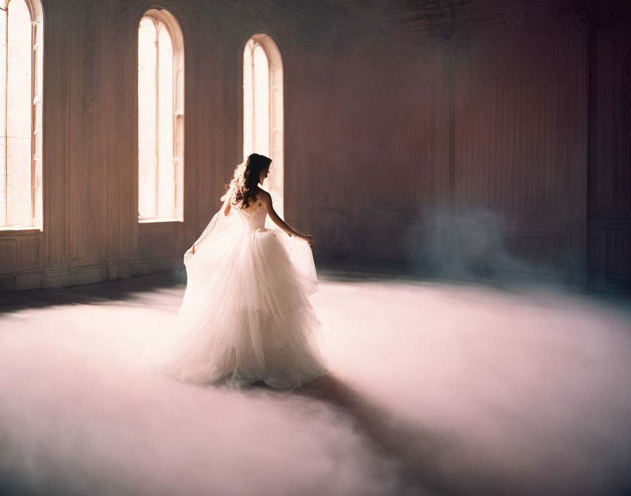 Bride twirls in flowing gown in sunlit room with mist