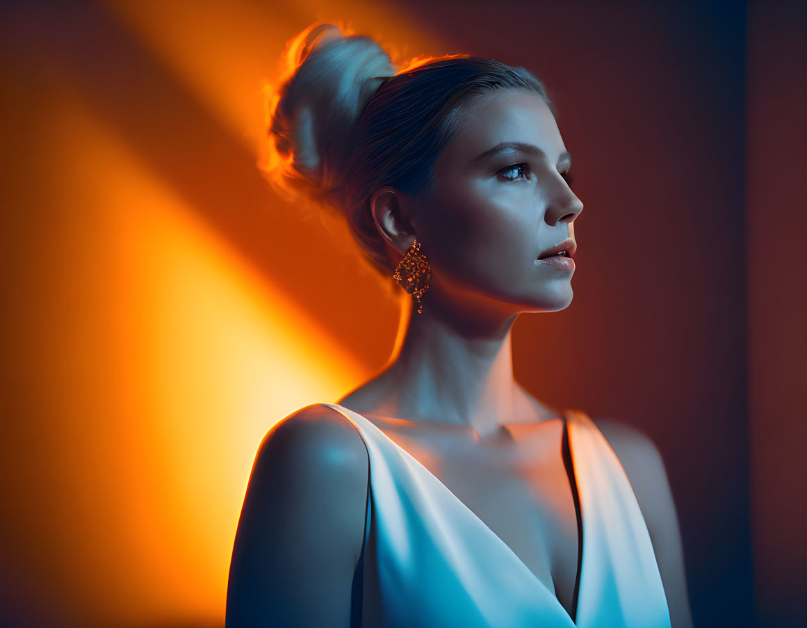 Woman in white dress with updo hairstyle and elegant earrings against warm gradient.