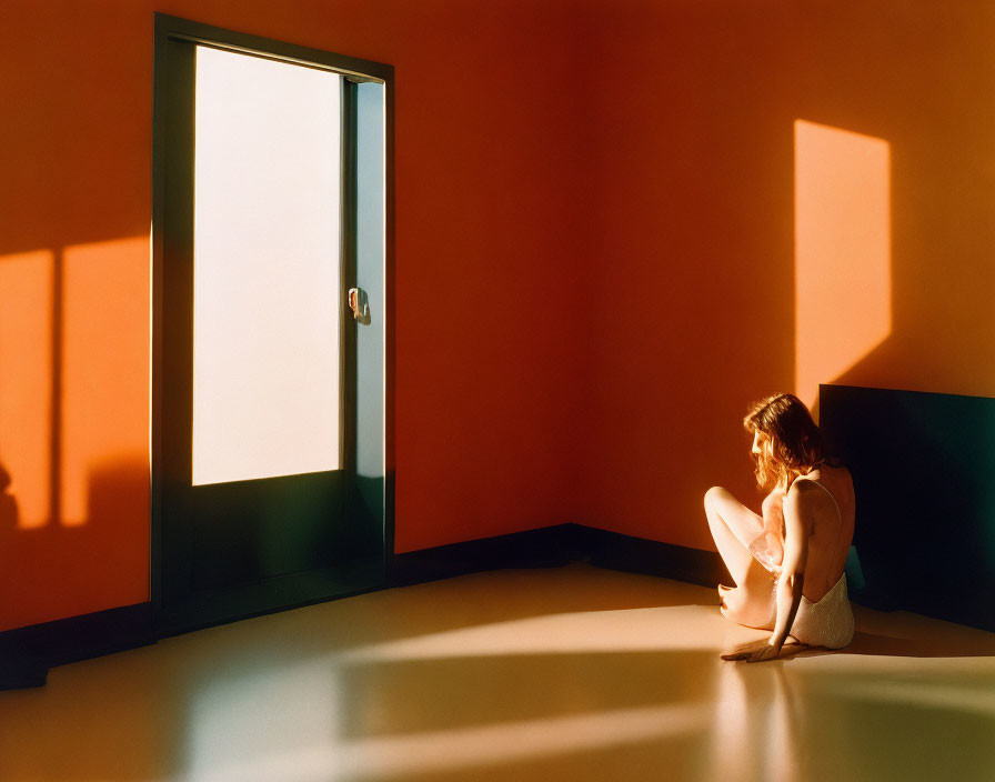 Person sitting by open door in room with orange walls and shadows.