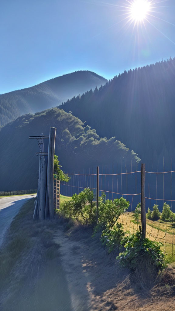 Sunlit scene with blue sky, fenced road, green mountains, and lens flare.