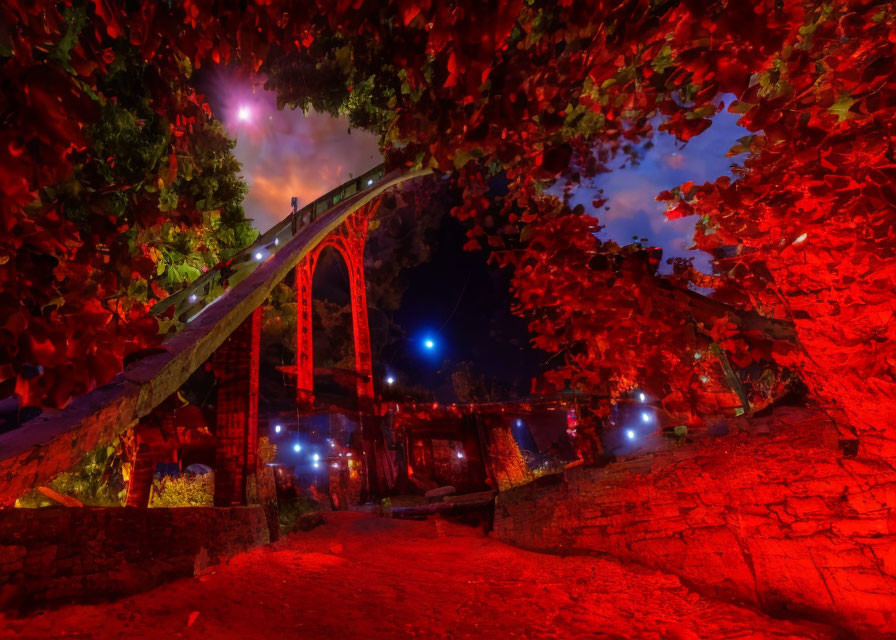 Vibrant night shot of arched bridge with red illumination and autumn leaves under starry sky