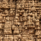 Ancient warrior faces carved on stone wall with ornate headdresses