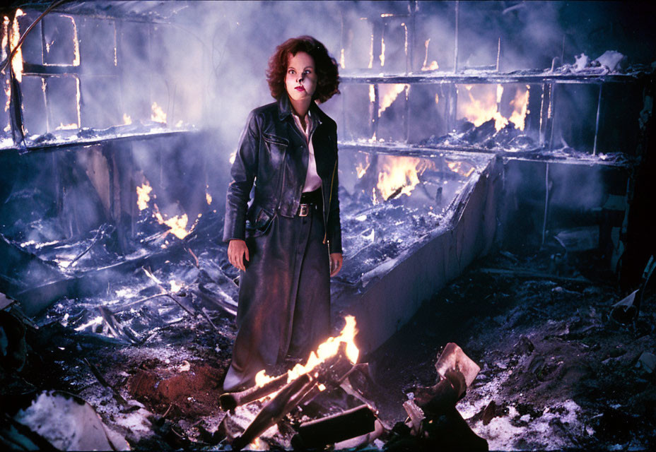 Intense woman in leather outfit by blazing fire in damaged building