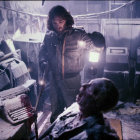 Person with flashlight in snowy, wrecked environment with cautious look and seated individual