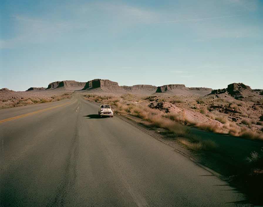 Desolate highway scene with solitary car, rocky landscape, and mesa formations