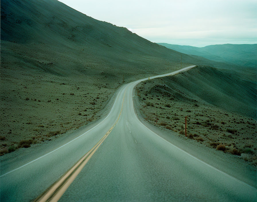 Barren hilly landscape with winding road under overcast sky