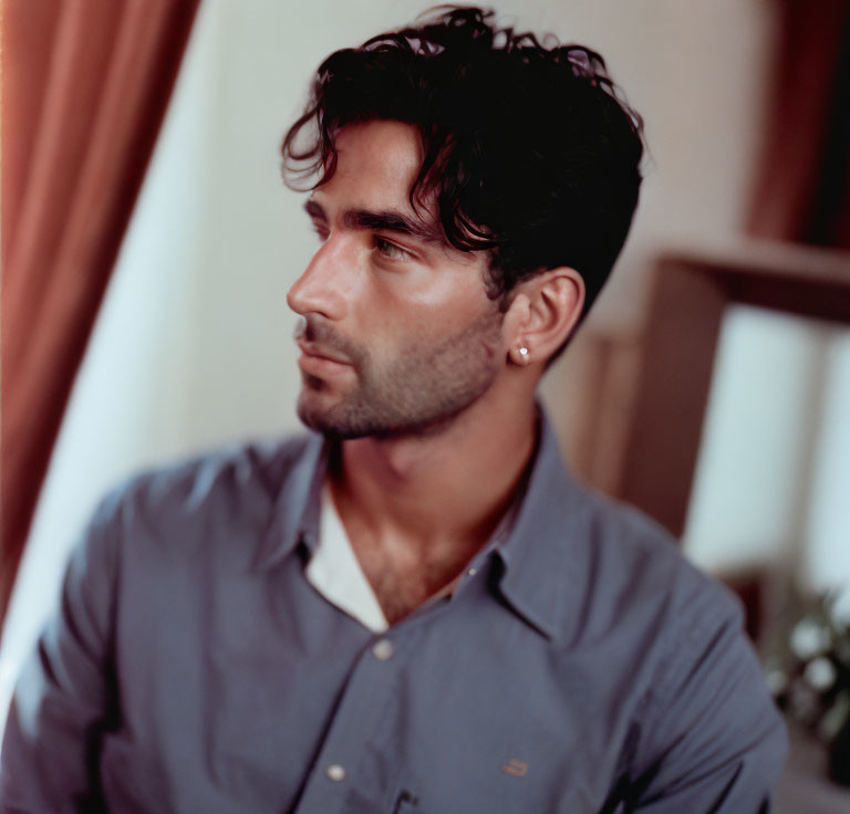 Dark-haired man in navy shirt with earring gazes right