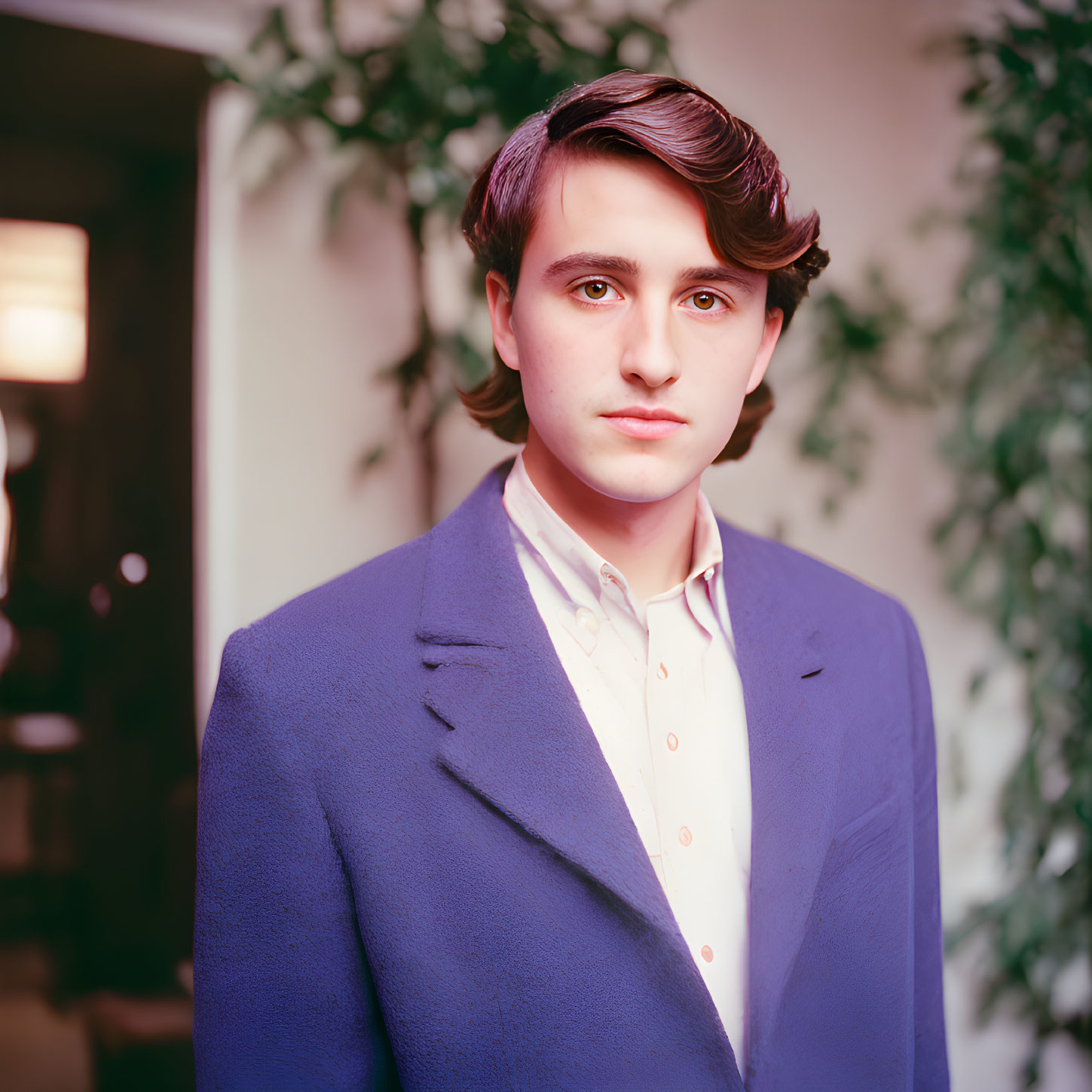 Dark-haired youth in blue blazer and open-necked shirt against green foliage