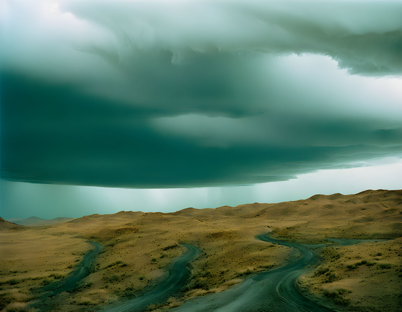 Desert hills with winding roads under stormy sky