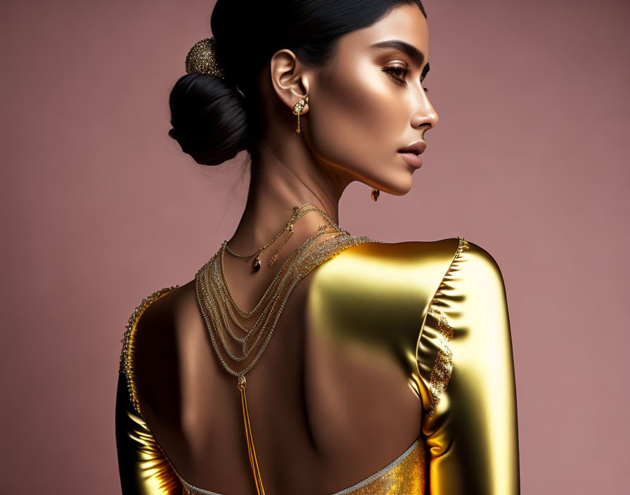 Elegant woman in gold dress with updo and jewelry on pink backdrop