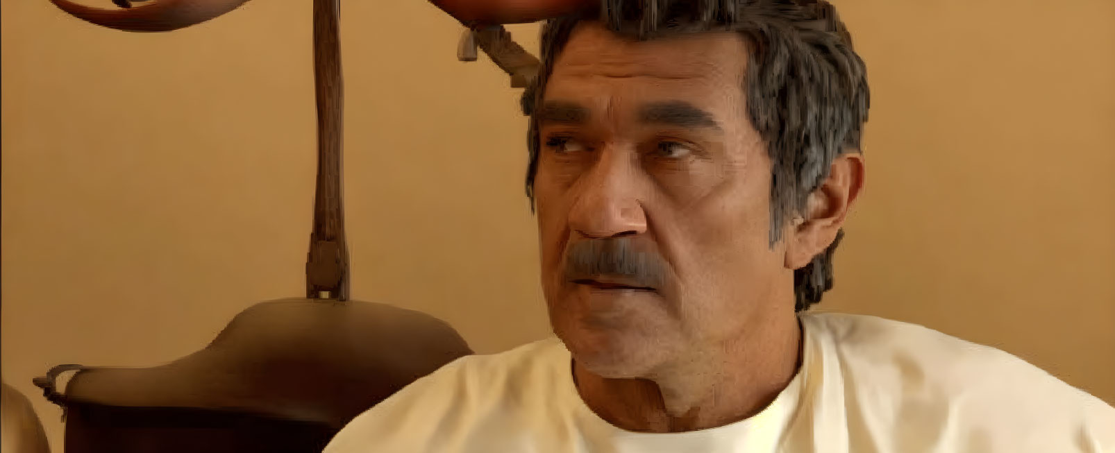 Middle-aged man with dark hair, mustache, and stubble in white shirt in room with beige