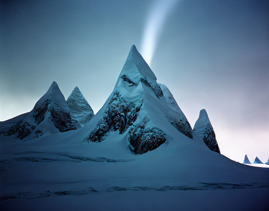 Snow-covered mountain range under twilight sky.