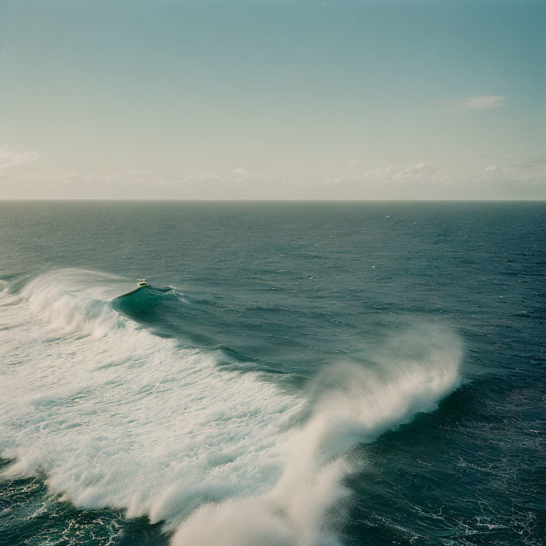 Boat riding large wave in vast calm sea under clear sky