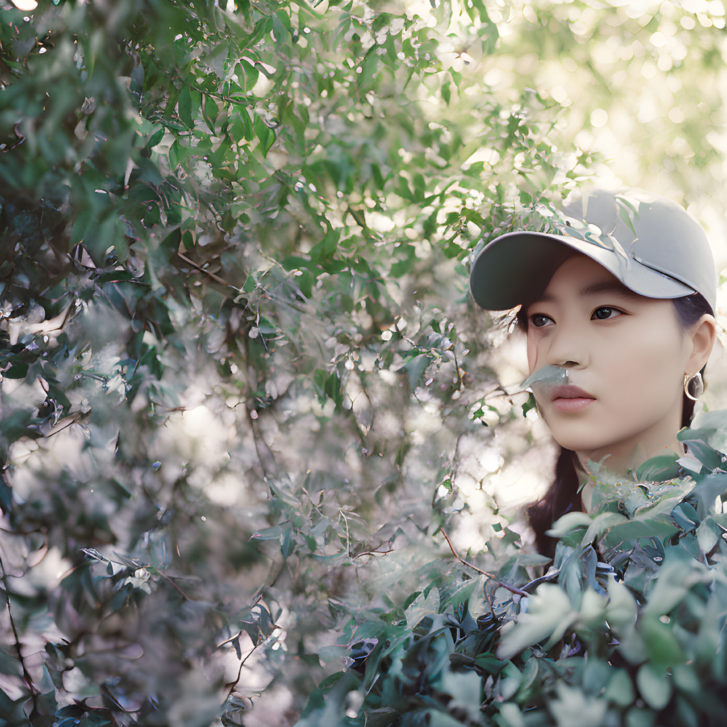 Person in cap gazes through sunlit green foliage