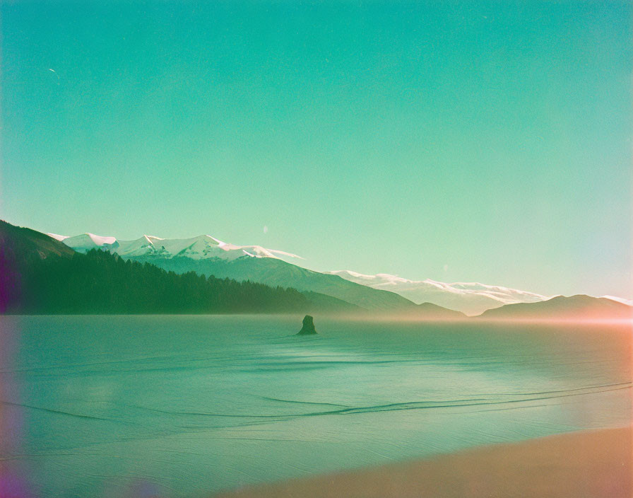 Tranquil lake with rock formation and snow-capped mountains