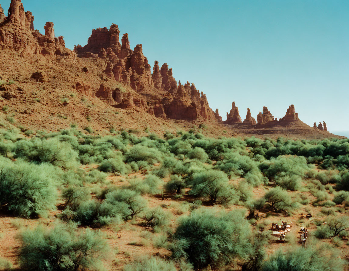 Desert landscape with red rock formations and green shrubs.