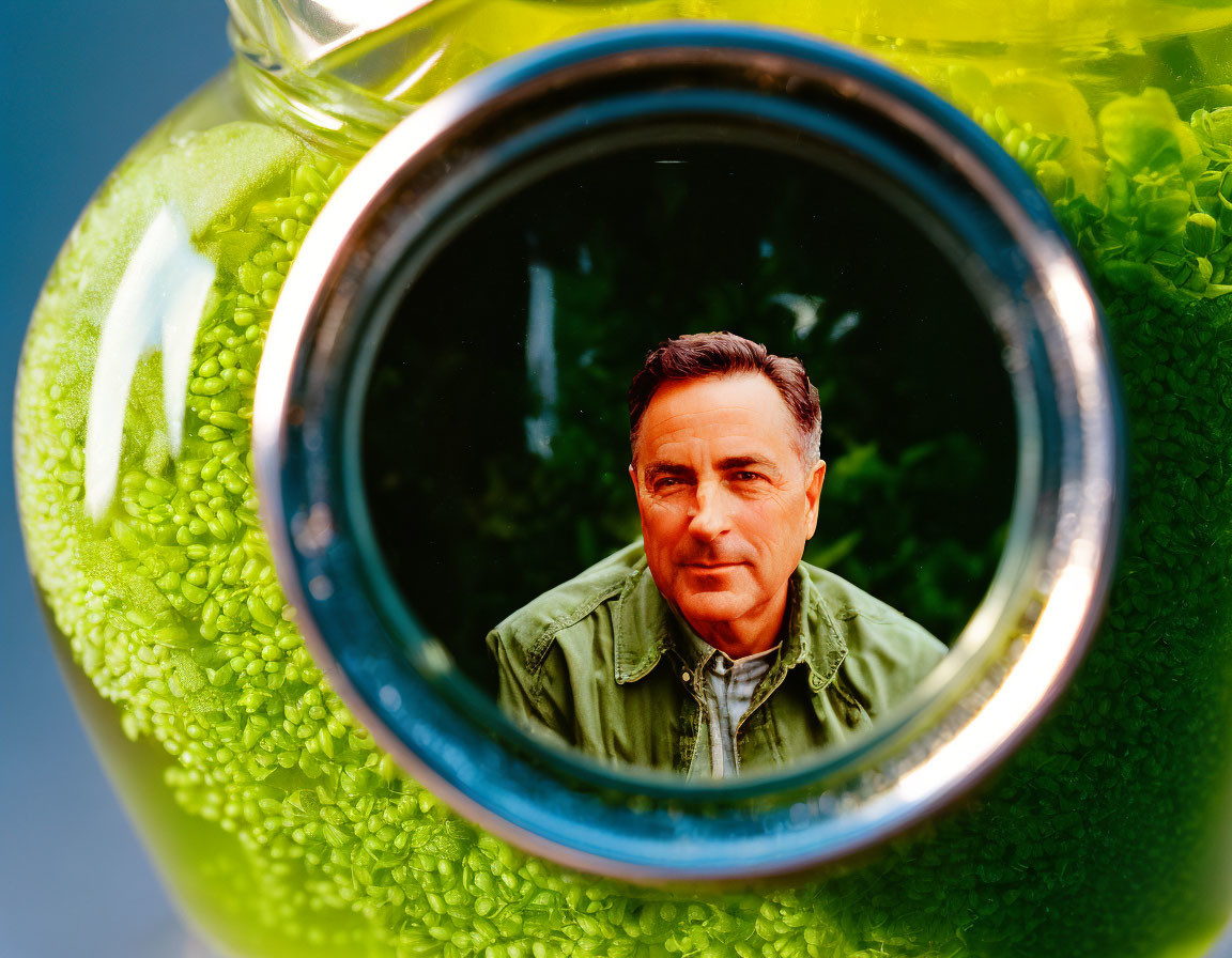 Clear jar with green contents distorting man's face.