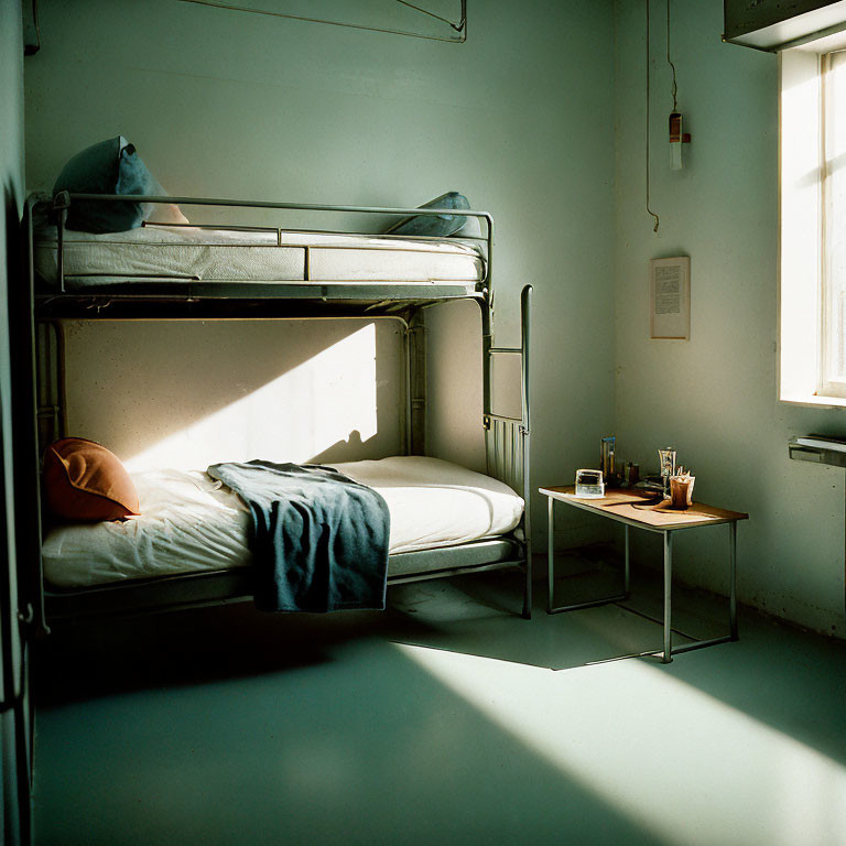 Simple bunk bed room with one bed made, light casting shadow.