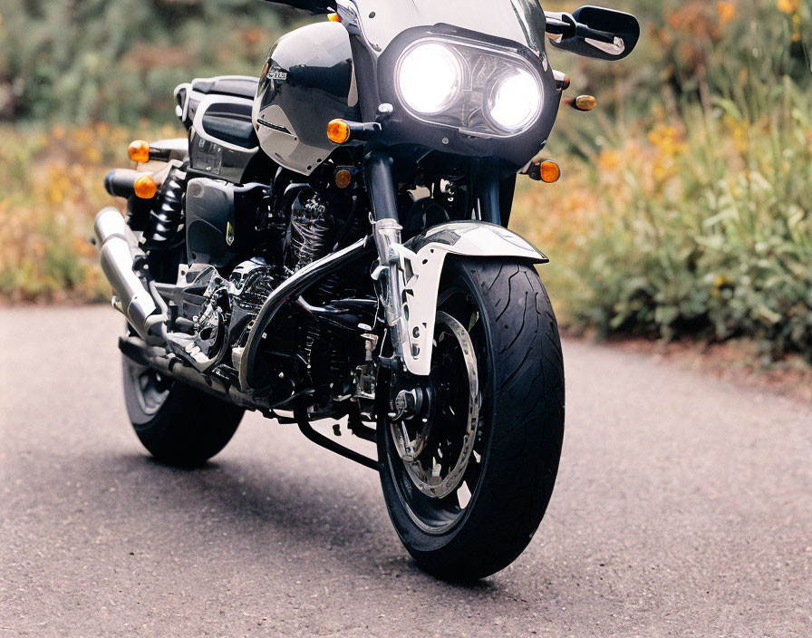 Black Motorcycle with Lit Headlights on Asphalt Road Amid Greenery