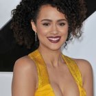 Woman in deep yellow dress and gold earrings holding an umbrella, styled with voluminous hair and red lipstick