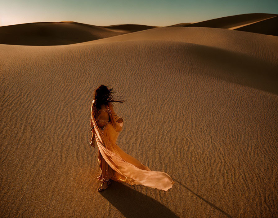 Person in flowing dress in sand dunes under warm golden light