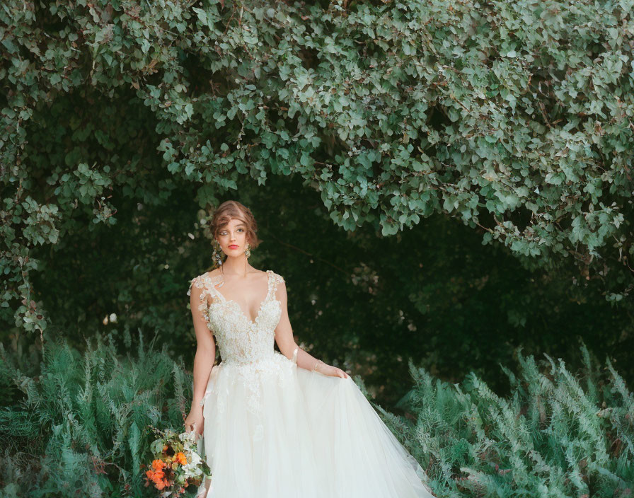 Elegant woman in wedding dress with bouquet against green backdrop