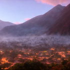 Morning mist shrouds village lights against mountain backdrop at dawn