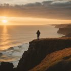 Person on Cliff at Sunset Overlooking Sea with Waves