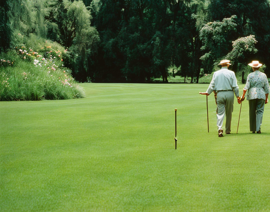 Elderly couple walking hand in hand on green lawn with flowers.