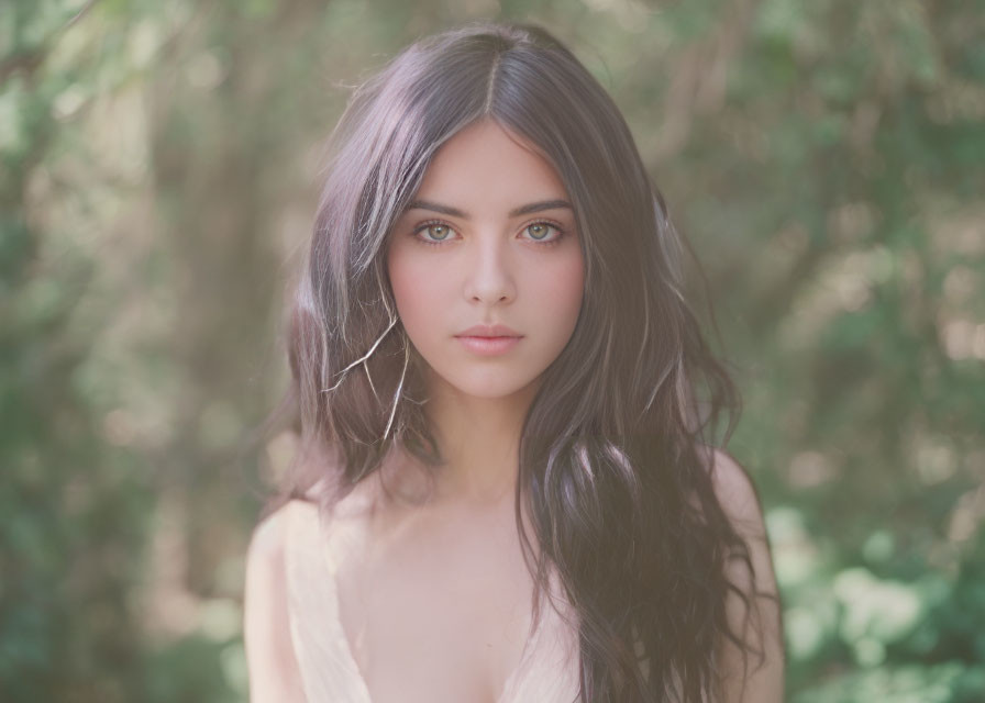 Dark-haired woman with striking eyes in front of blurred green background