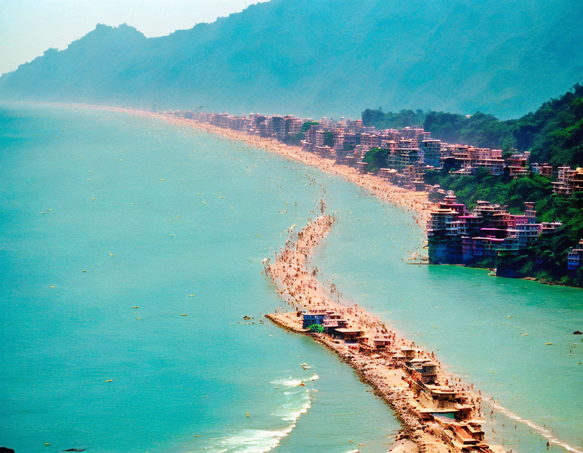 Crowded beach and coastal city with green mountains under clear sky