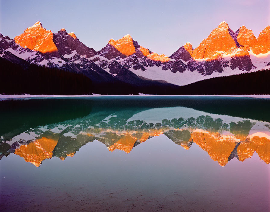 Scenic alpenglow on mountain peaks reflected in serene lake at twilight