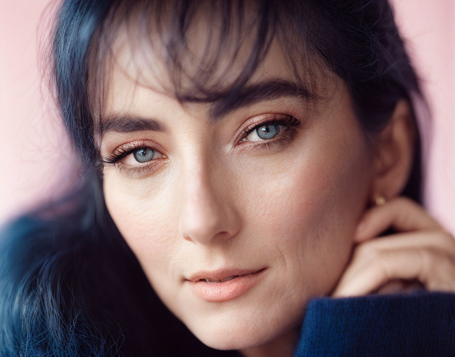 Close-up portrait of woman with blue hair and blue eyes against pink background