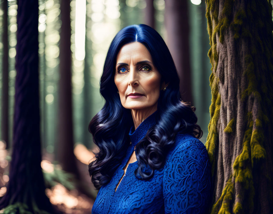 Dark-haired woman in blue dress standing in forest with sunlight filtering through trees