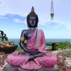 Seated Buddha statue in meditation by the ocean with pink fabric and lanterns