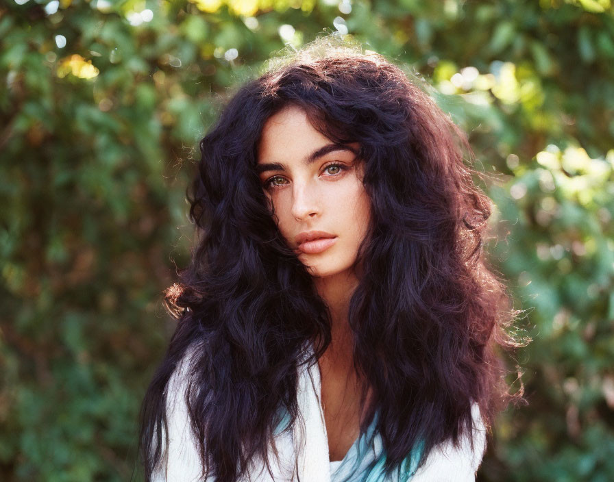 Dark-haired woman with striking features in garden with sunlight filtering through foliage