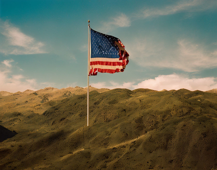 American flag waving on pole over dry hills and cloudy sky