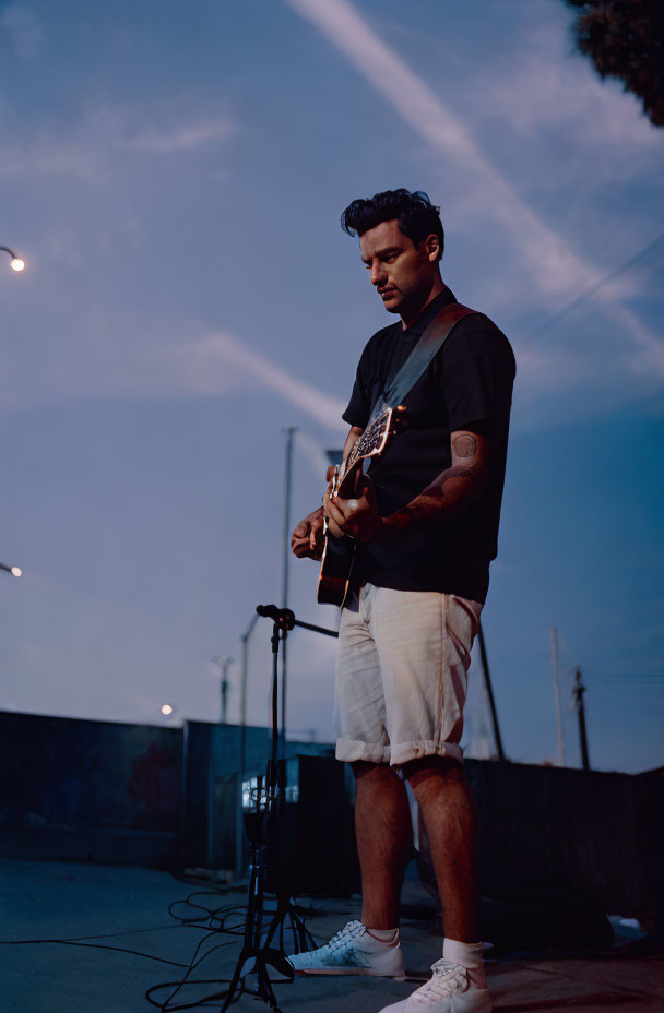 Man playing acoustic guitar outdoors at twilight