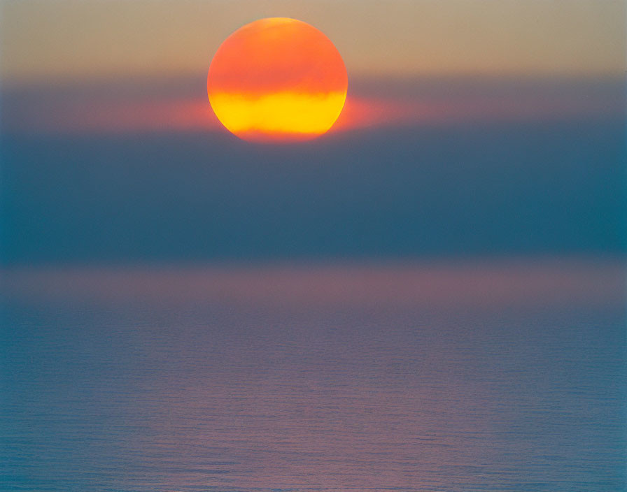 Vivid orange sun setting over calm ocean horizon