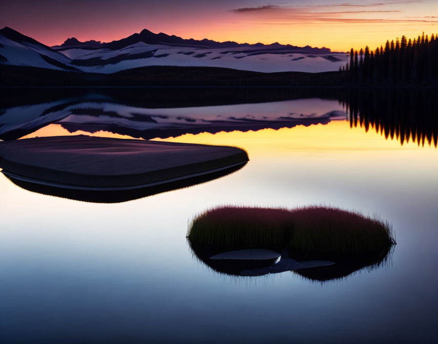 Scenic sunset lake with mountain silhouettes and grassy islet